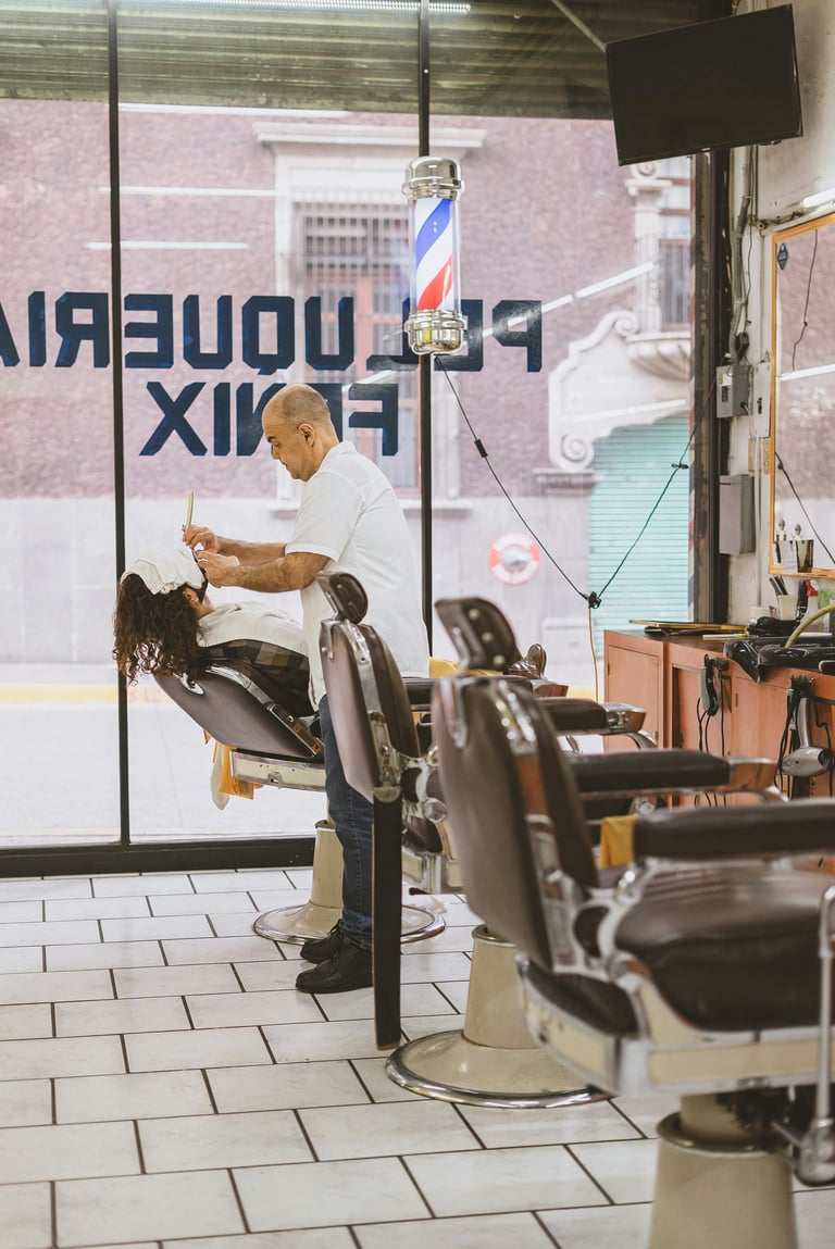 Barber giving a haircut to a customer in a traditional barber shop with vintage chairs and barber pole visible